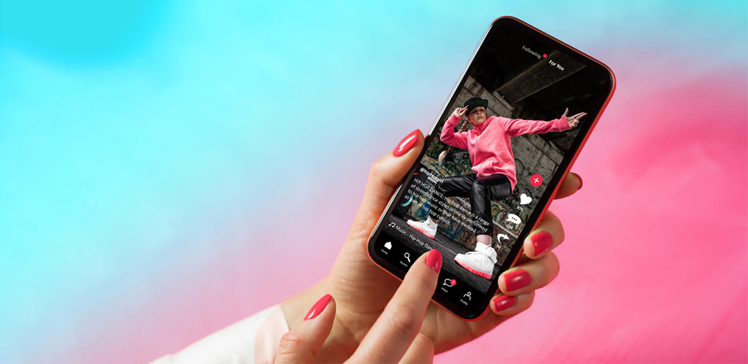 mobile phone showing the tiktok app with a person in a pink hoodie dancing