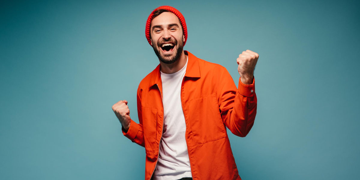 a happy man wearing a bright orange jacket punching his fists into the air with glee