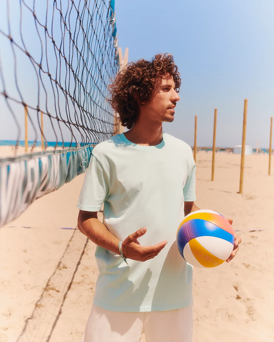 young man playing volleyball on the beach wearing a Crafter t-shirt in caribbean blue