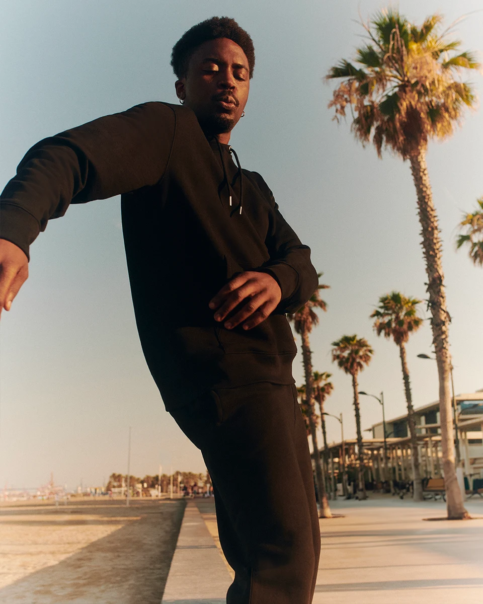 model wearing a black hoodie dancing under palm trees