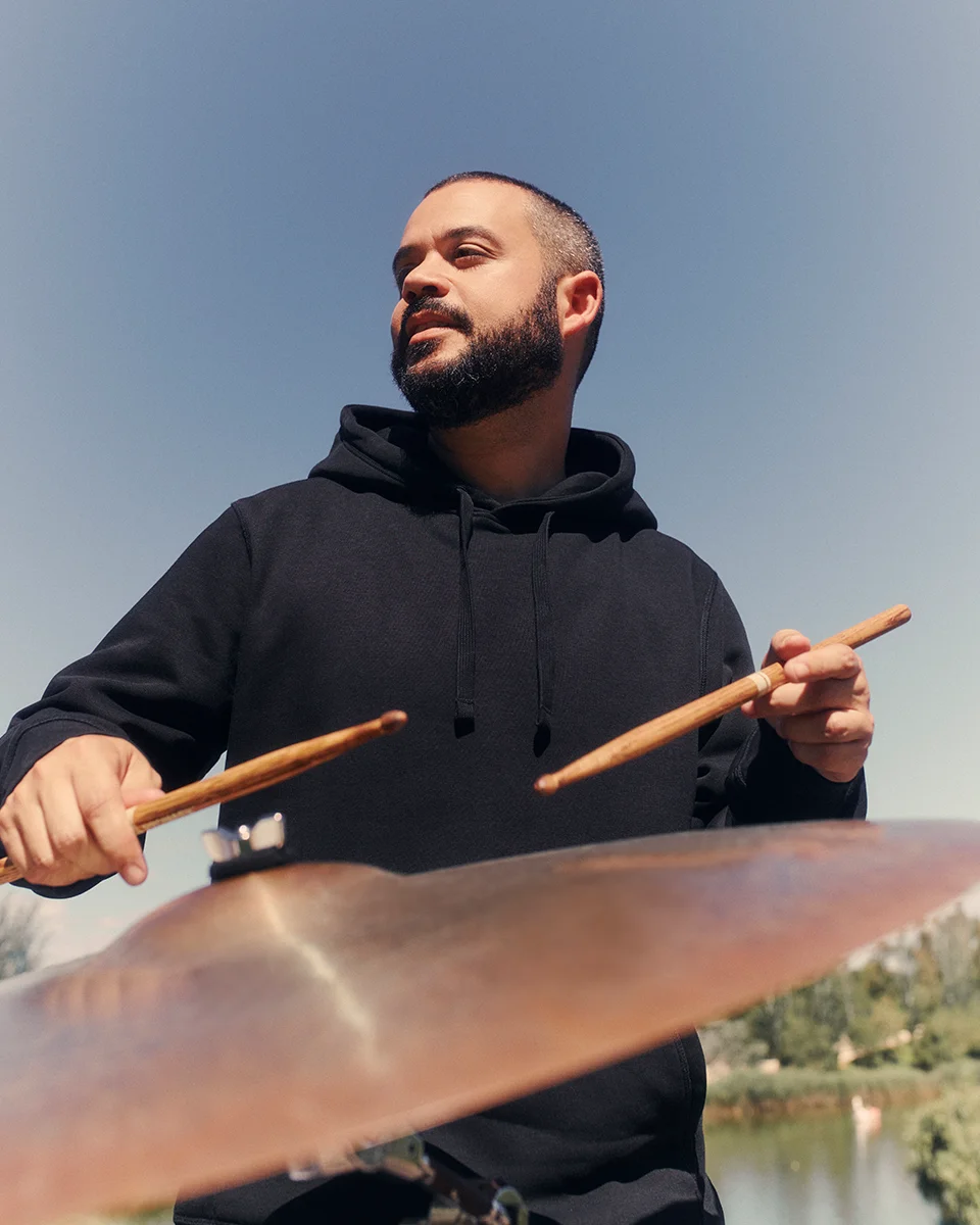 bearded man playing the drums wearing a black drummer hoodie
