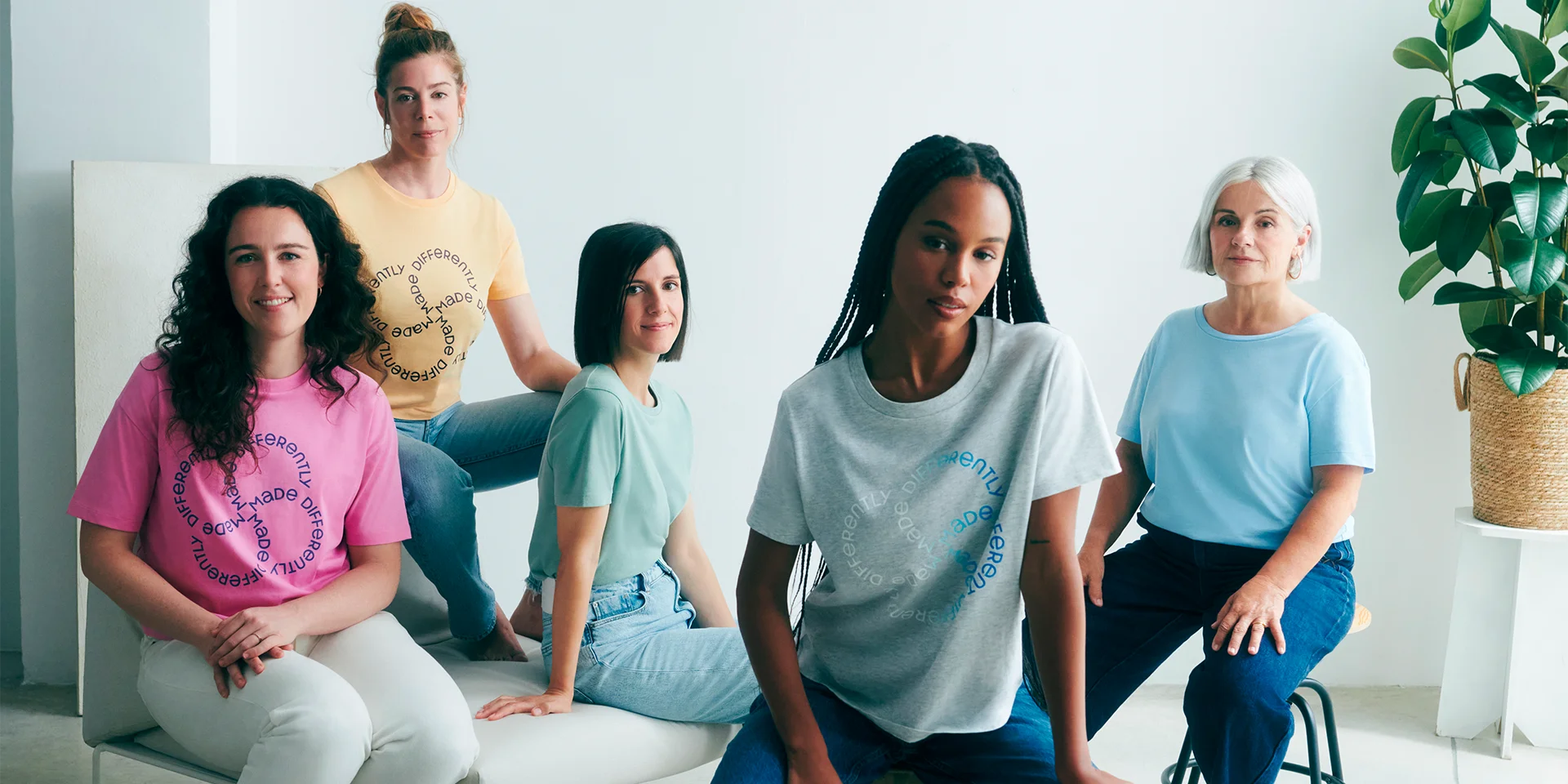 five women sat smiling together and wearing matching t-shirt styles in a variety of pastel shades