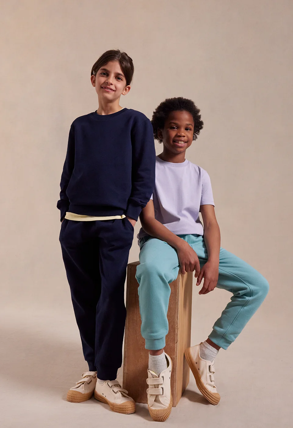 two fashionable kids sat on stools wearing matching joggers and t-shirts